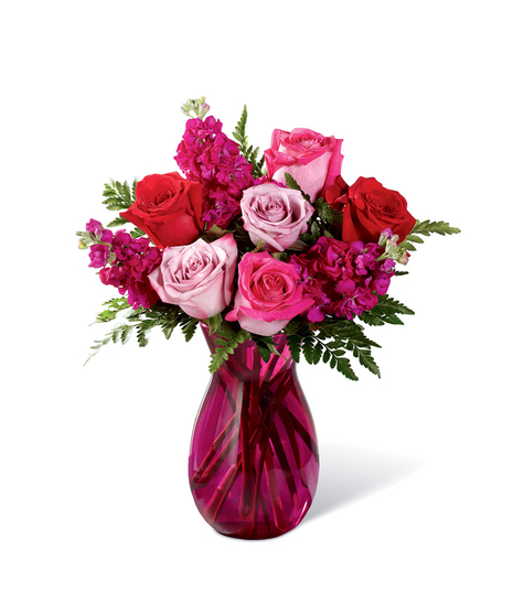 Hot pink, red, and lavender roses accented with lush greens while seated in a vibrant pink glass vase.