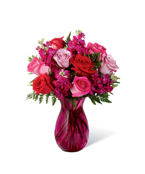 Hot pink, red, and lavender roses accented with lush greens while seated in a vibrant pink glass vase.