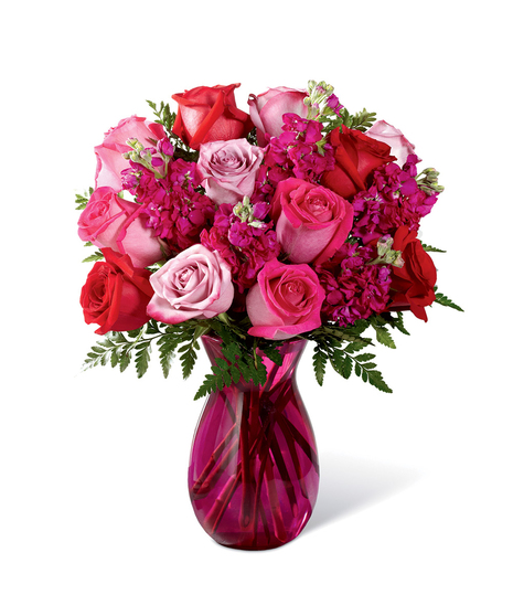 Hot pink, red, and lavender roses accented with lush greens while seated in a vibrant pink glass vase.